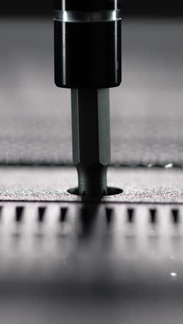 macro view of driver bit tightening a single screw into perforated panel of an electronic device