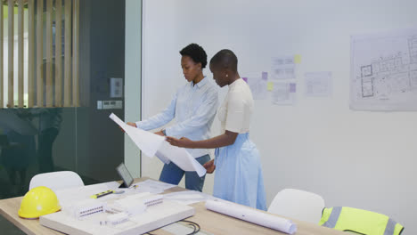 two african american female architects in discussion studying blueprints in office