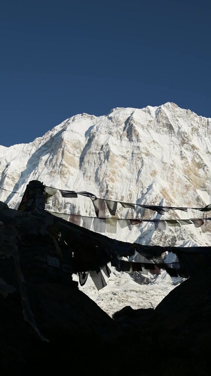 Primo piano verticale di bandiere di preghiera nelle montagne del Nepal, video verticale per social media, Instagram Reels e TikTok di colorate bandiere di preghiera tibetane sotto un cielo blu e soleggiato negli innevati Himalaya