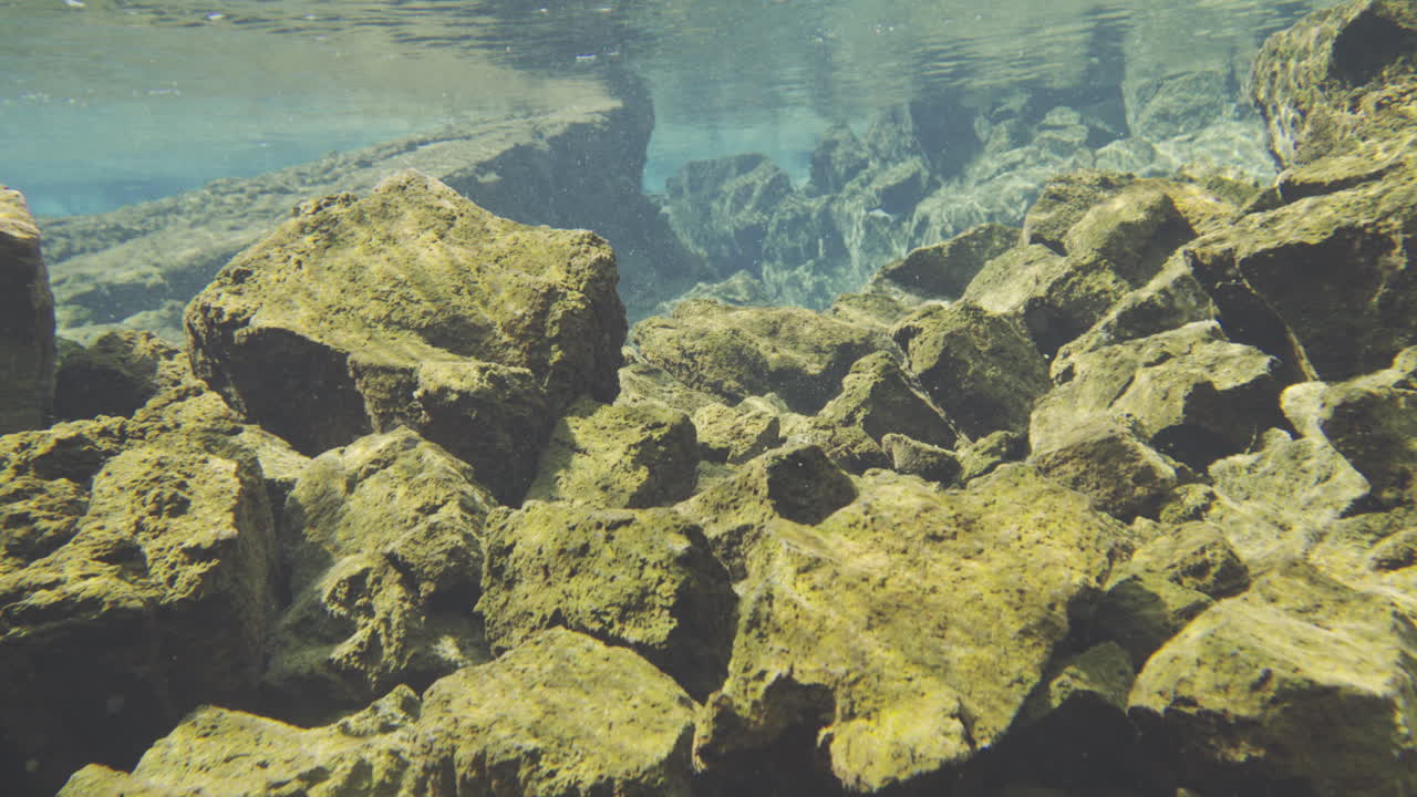 Move with the water over rocks in underwater exploration of rocky terrain in a clear freshwater environment during daylight hours Silfra fissure iceland