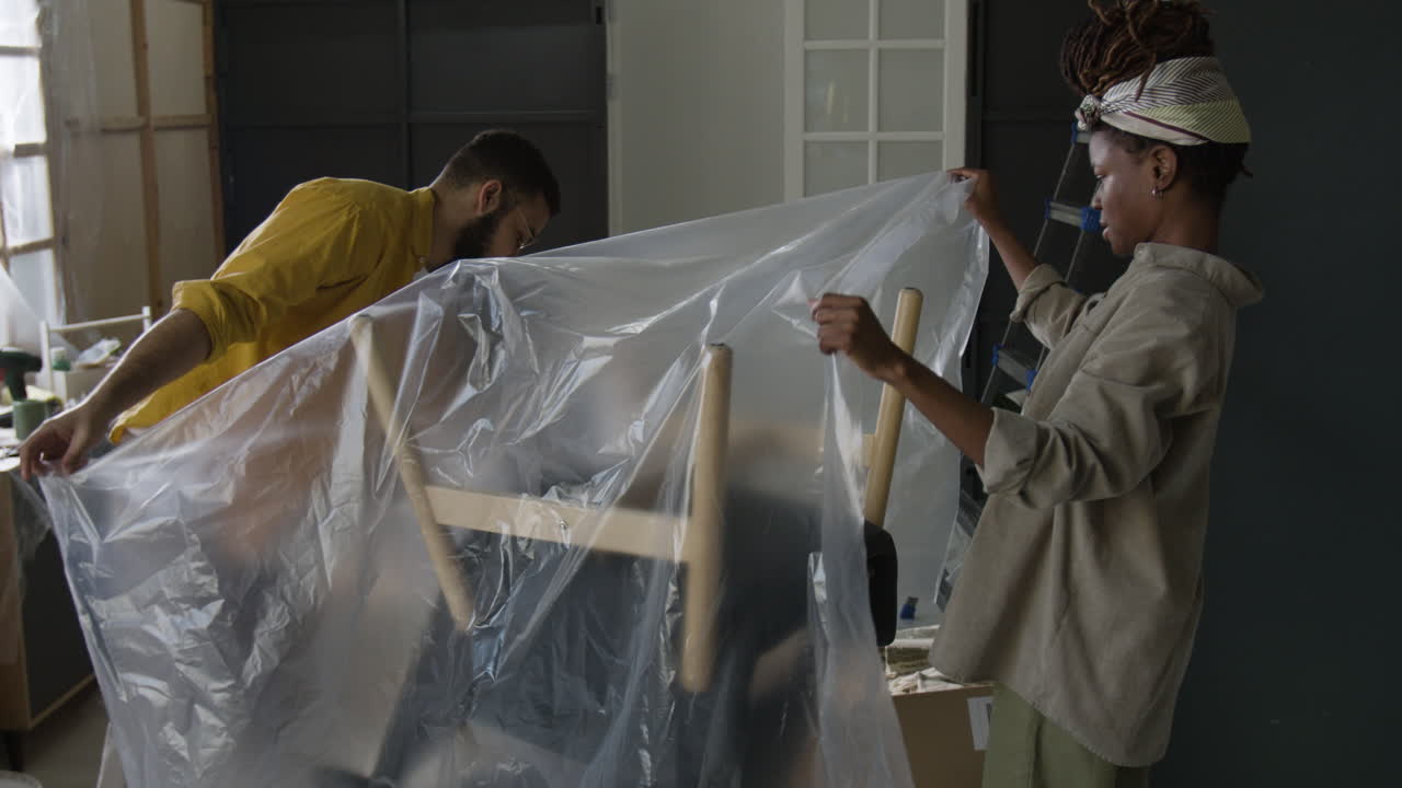 Couple moving furniture and wrapping it in plastic