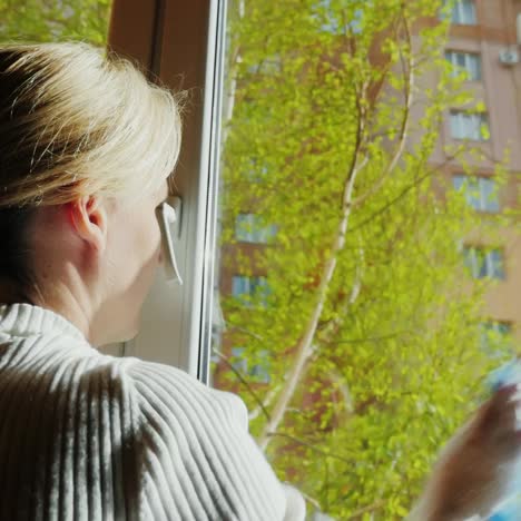 a young woman washes a window in her apartment