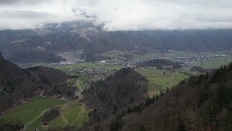 Aerial-estabilshing-overview-descends-along-ridgeline-forests-with-green-meadows-in-valleys-and-peaceful-European-town