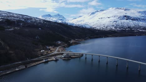 Stunning-aerial-orbit-of-snowy-mountain-landscape-and-scenic-Arsteinbrua-Bridge-in-Gratangen,-Norway