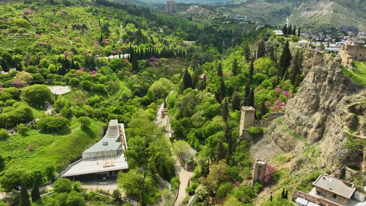A sweeping drone view of the historic Narikala Fortress surrounded by greenery and the hills of Tbilisi, Georgia