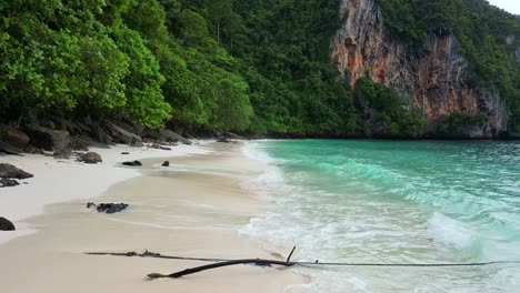 a serene beach scene featuring soft white sand, clear turquoise waters, and lush green cliffs in the background.
