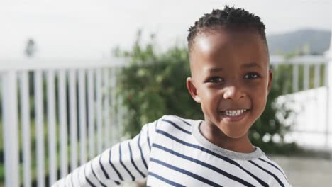 portrait of happy african american boy smiling on sunny terrace, slow motion
