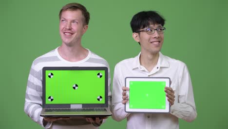 two happy young multi-ethnic businessmen showing laptop and digital tablet to the camera