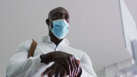 African-american-businessman-in-face-mask-disinfecting-hands-in-office