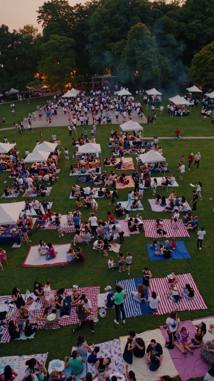 Groups of people enjoying picnics on blankets and under gazebo tents in a park during sunset, fostering a vibrant and festive atmosphere filled with laughter and connection