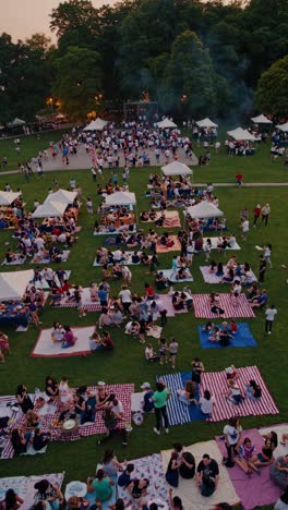 groups of people enjoying picnics on blankets and under gazebo tents in a park during sunset, fostering a vibrant and festive atmosphere filled with laughter and connection