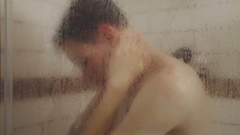 portrait of a man behind glass shower cabin taking a bath