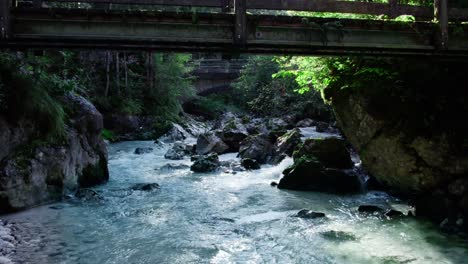 aerial flying along forest mountain stream rapids under wooden small bridge