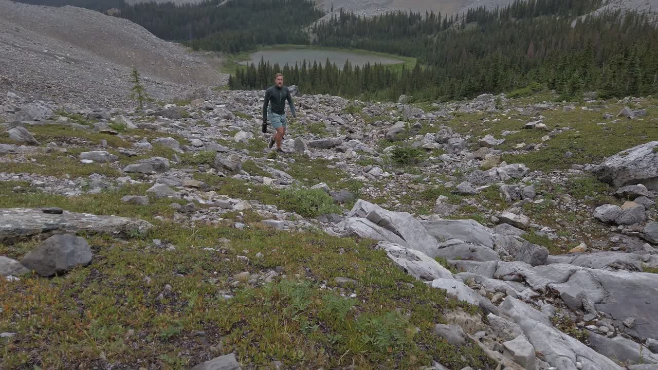 Hiker walking up mountain with lake and forest circling Rockies Kananaskis Alberta Canada