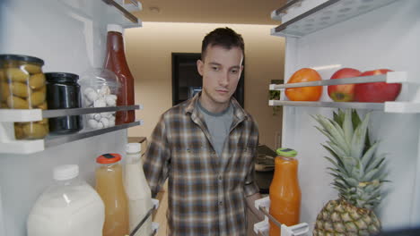 Un-Joven-Saca-Un-Recipiente-Con-El-Desayuno-Del-Frigorífico.-Vista-Desde-El-Interior-Del-Refrigerador