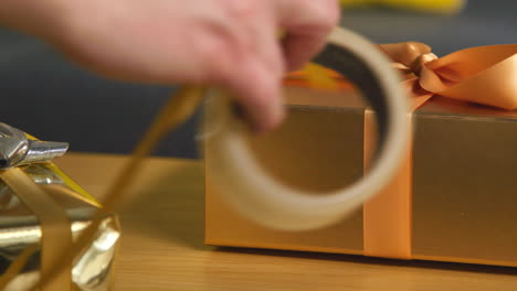 close up of person gift wrapping present on table at home with wrapping paper and sticky tape