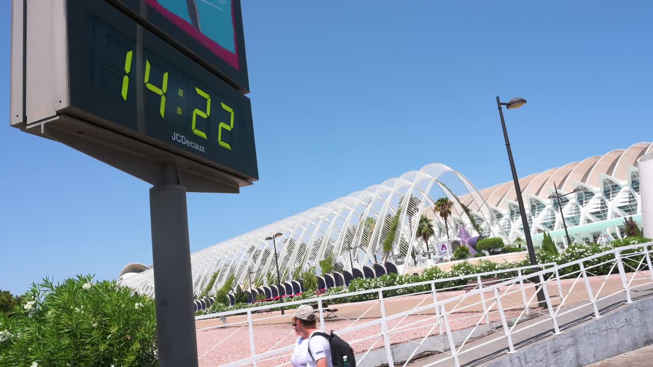 Tourists walk past a digital thermometer displaying a temperature of 39 degrees Celsius (39°C) outside the City of Arts and Sciences complex during the summer tourist season in Valencia, Spain.