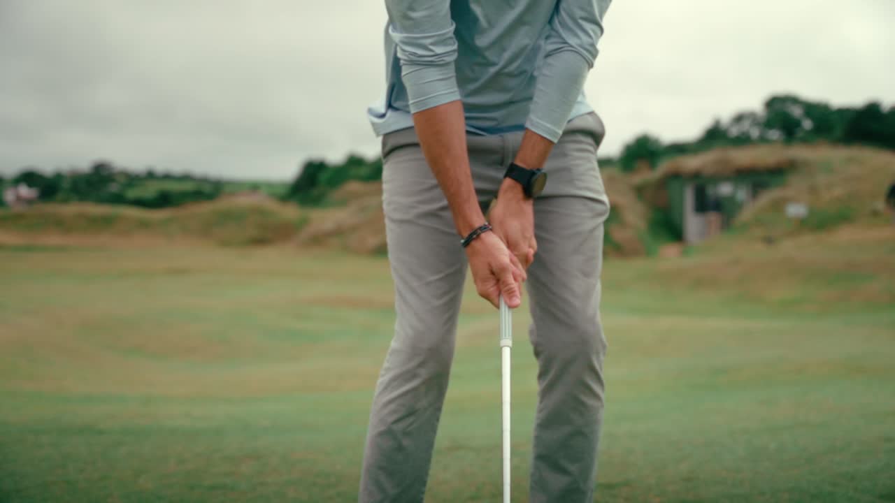 Male golfer sets up shot, lines up wedge club behind ball for chip shot on rolling hilly fairway of Ireland links golf course