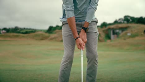 male golfer sets up shot, lines up wedge club behind ball for chip shot on rolling hilly fairway of ireland links golf course