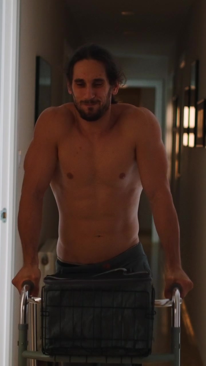 Uomo a torso nudo che usa un deambulatore per la riabilitazione in un corridoio.