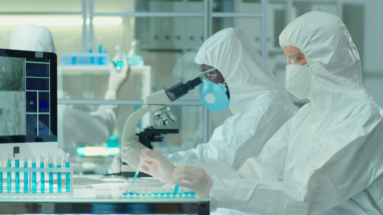 Multiethnic Scientists in Protective Uniforms Working Together in Laboratory
