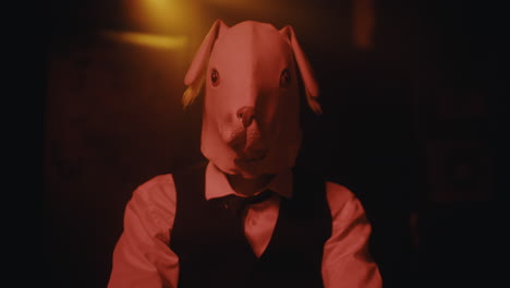man in a pig mask holding cards in a dark room