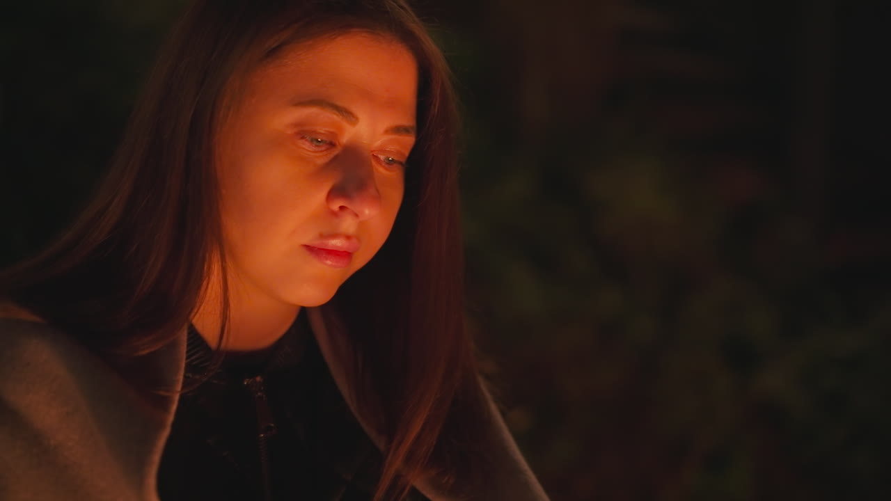 mujer calentándose con el fuego por la noche. dama deprimida mirando la hoguera ardiendo con expresión triste en el patio. devastación por la soledad y la depresión