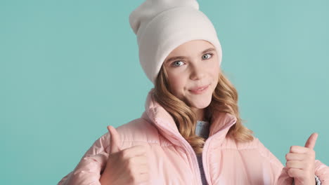 teenage caucasian girl with winter clothes and thumbs up in front of the camera.