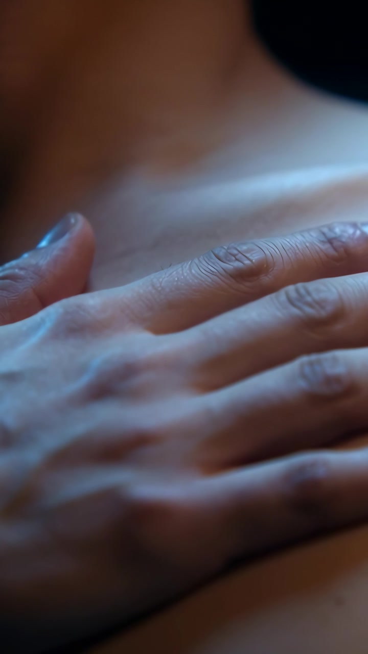 Vertical video: Comforting painted-nail hand stroking upper chest in warm light room, showing strap