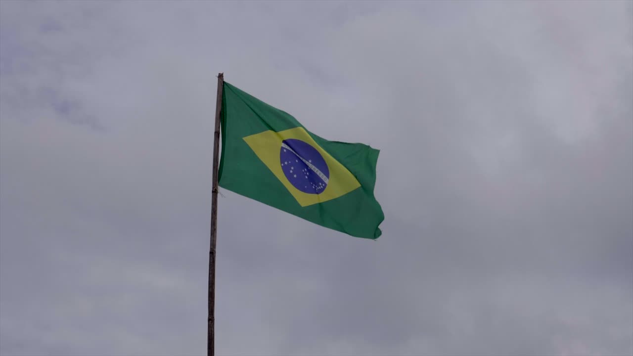 Bendera Brasil di tiang berkibar tertiup angin di bawah langit mendung berawan