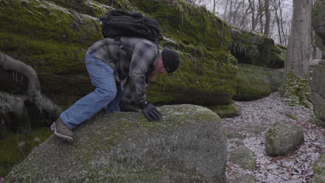 disparo en cámara lenta de un excursionista con una mochila saltando sobre una roca mosey con musgo cubierto formaciones glaciares rocosas con raíces de árboles creciendo en el bosque boscoso