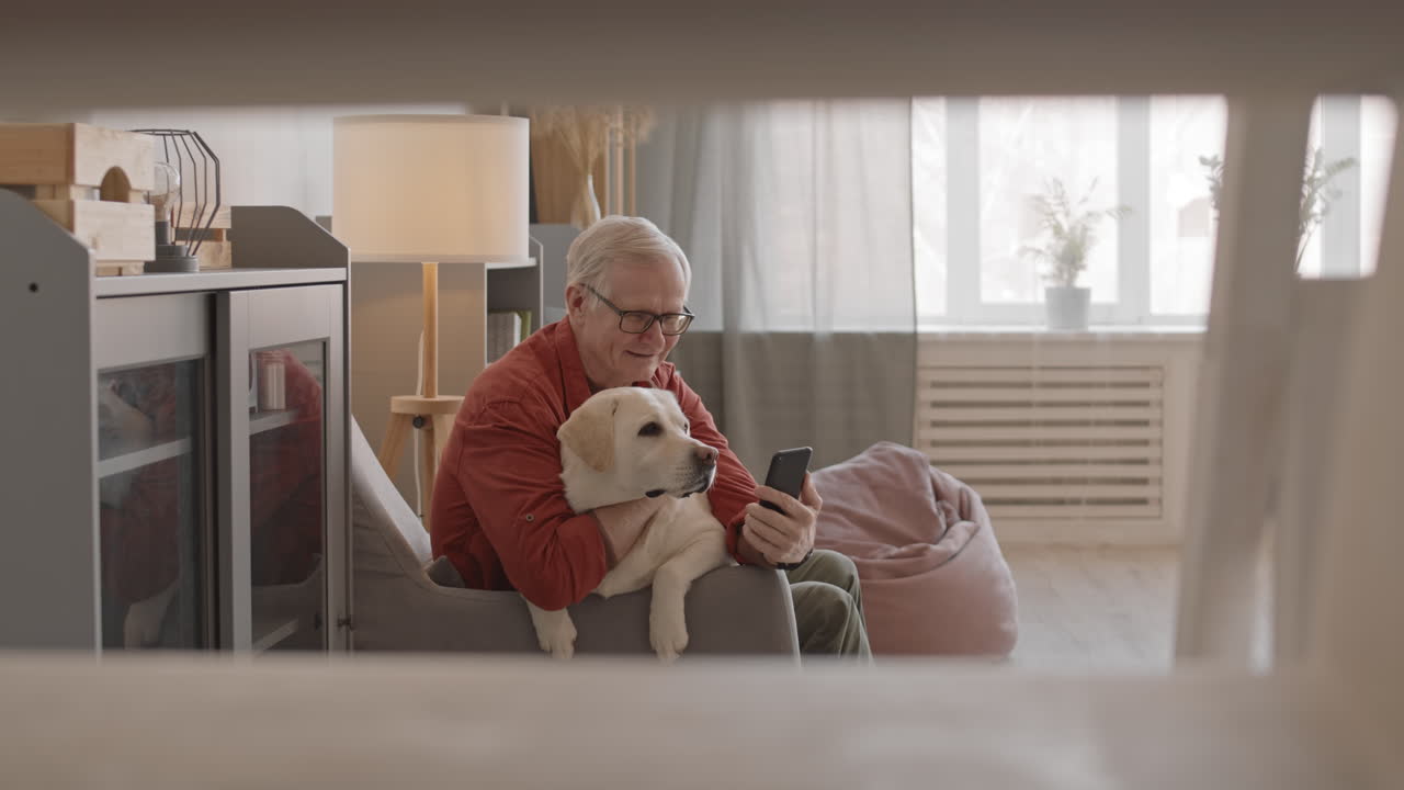 Elderly Man with Dog Video Calling on Smartphone at Home