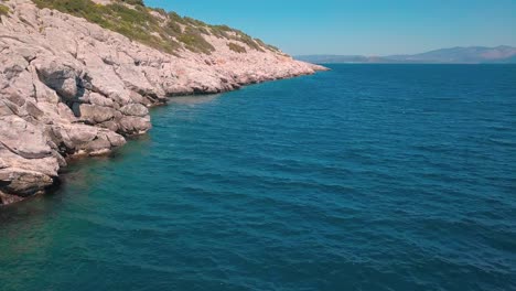 slow forward and crane down drone shot next to a rocky shore in the aegean sea, greece