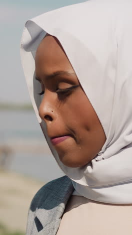 sorrowing african-american woman with headscarf stands on embankment closeup slow motion. unhappy muslim lady at riverside. heartbroken person portrait