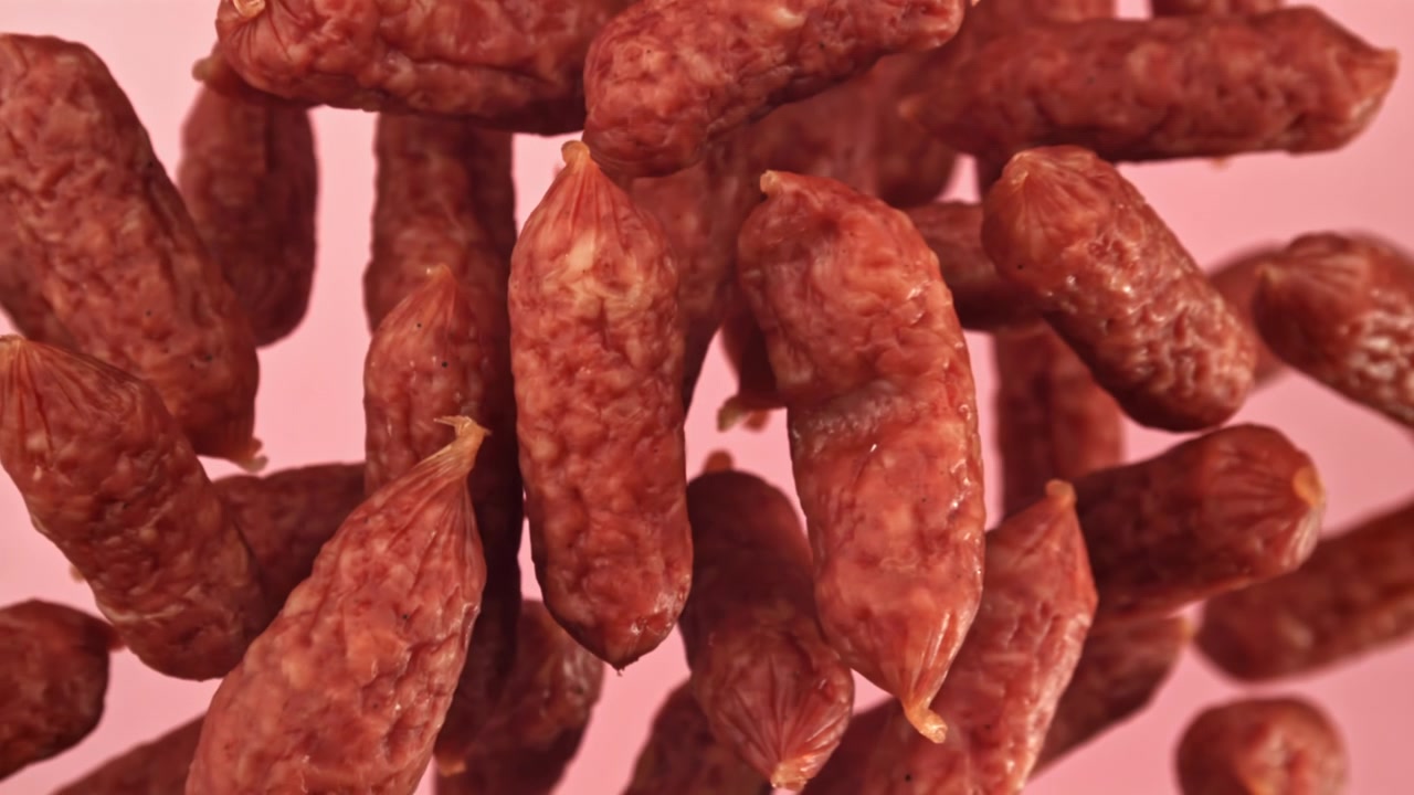 Primo piano di mini salami che cadono al rallentatore su sfondo rosa