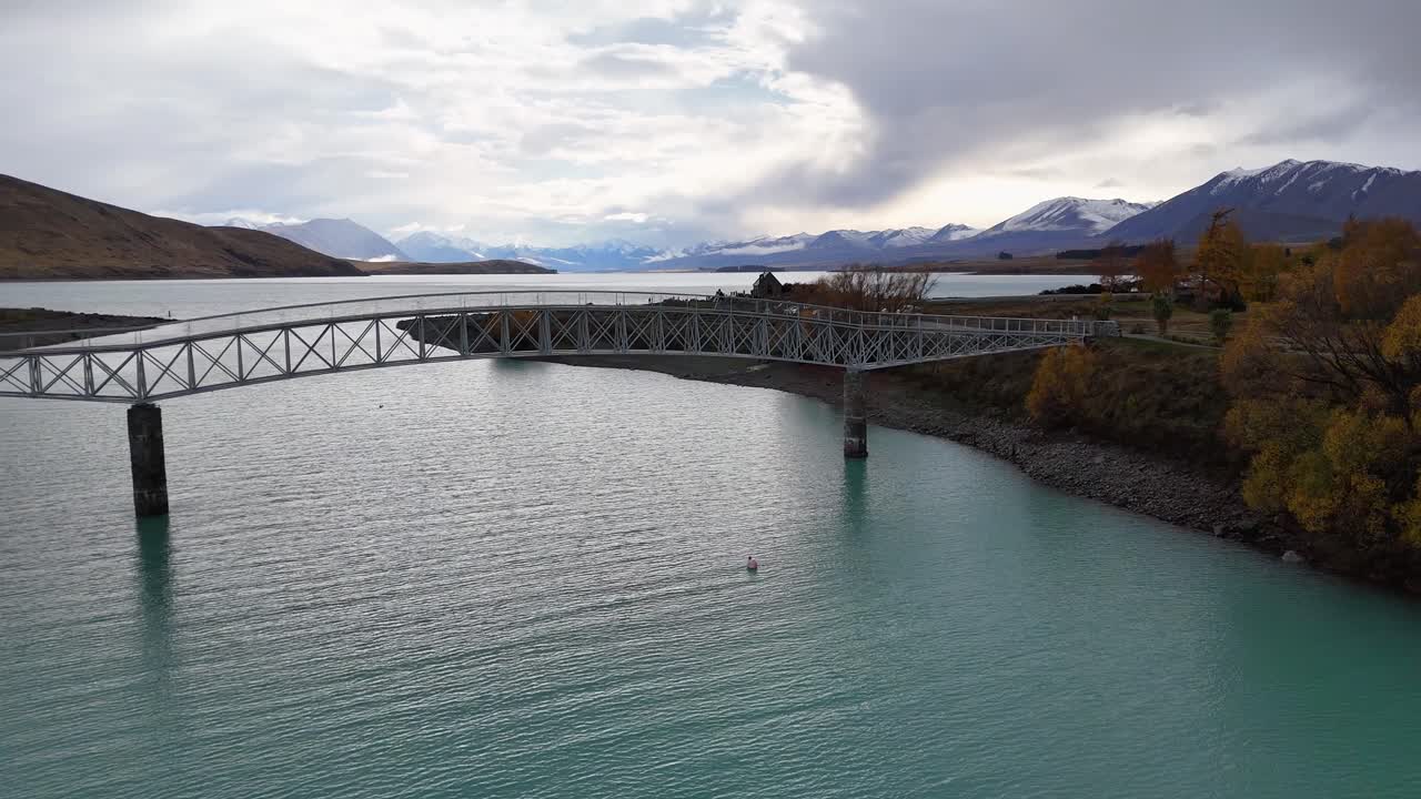 Aerial video captures Lake Tekapo's serene landscape, highlighting a bridge, turquoise waters, and surrounding mountains under soft, diffused lighting