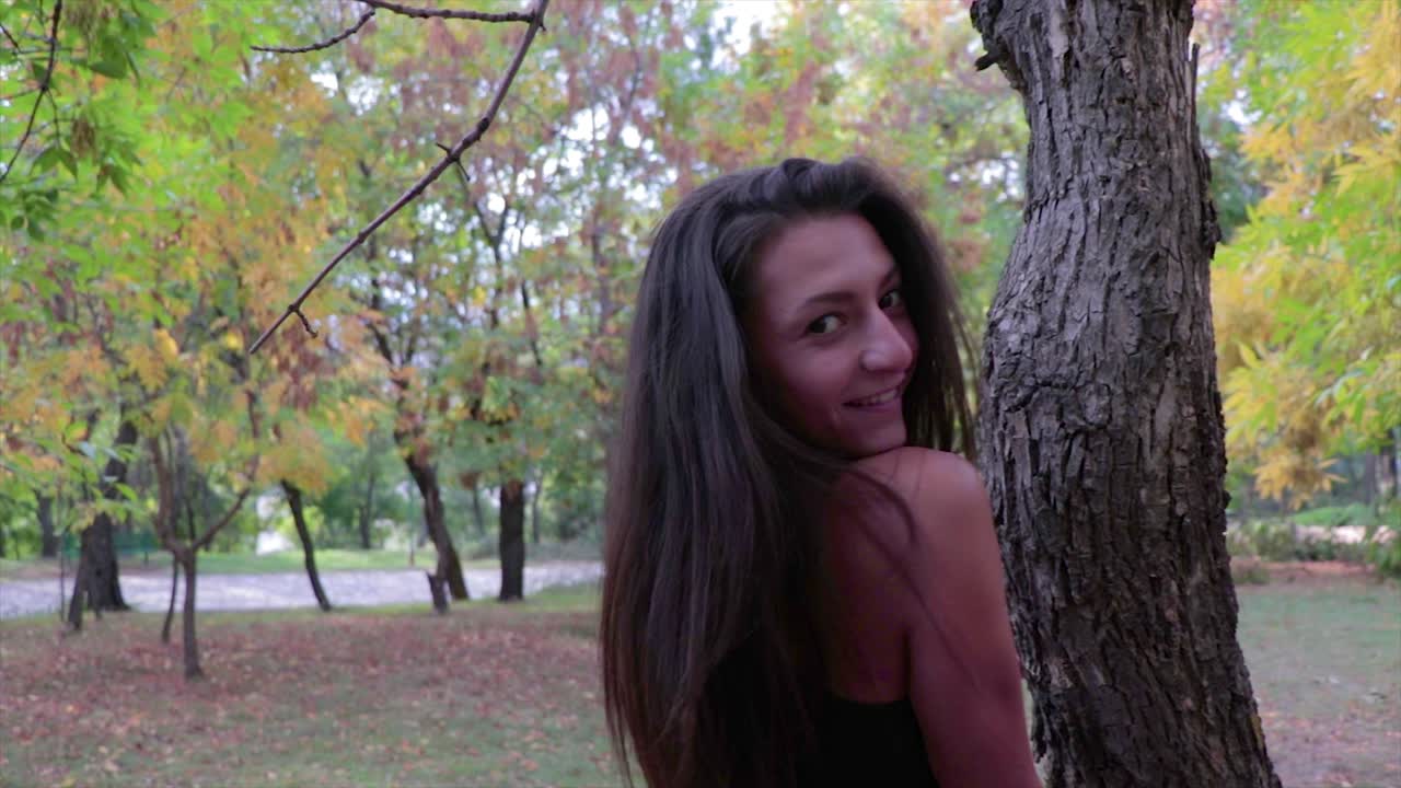 chica modelando alrededor de un tronco de árbol en cámara lenta