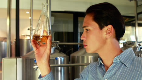 smiling man examining beer in flask 4k