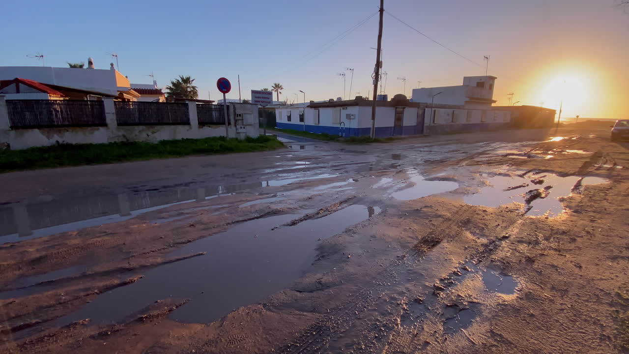 Pozzanghere e strada fangosa che riflettono la luce del tramonto in un quartiere costiero vicino alla spiaggia di Costa Ballena