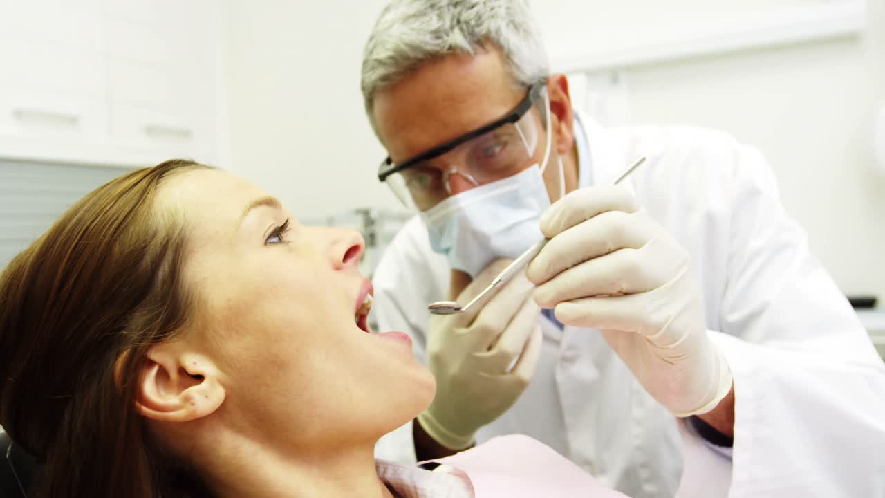 Dentist examining a female patient with tools