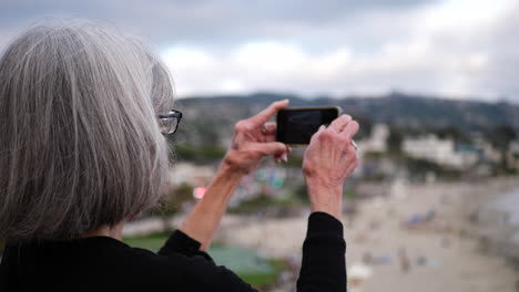 una viajera de mediana edad tomando una foto con su teléfono de la ciudad y el océano en laguna beach, california a cámara lenta