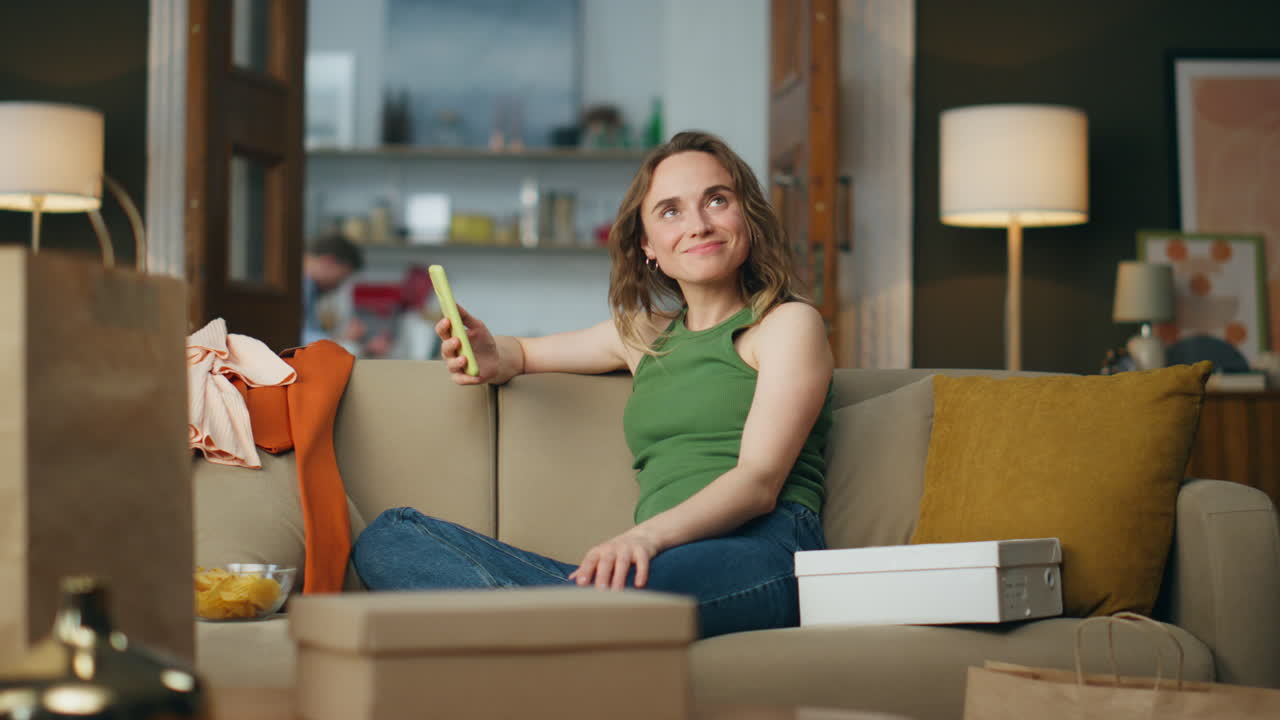 una adicta a las compras satisfecha con un teléfono móvil en una casa desordenada. una mujer despreocupada pensando