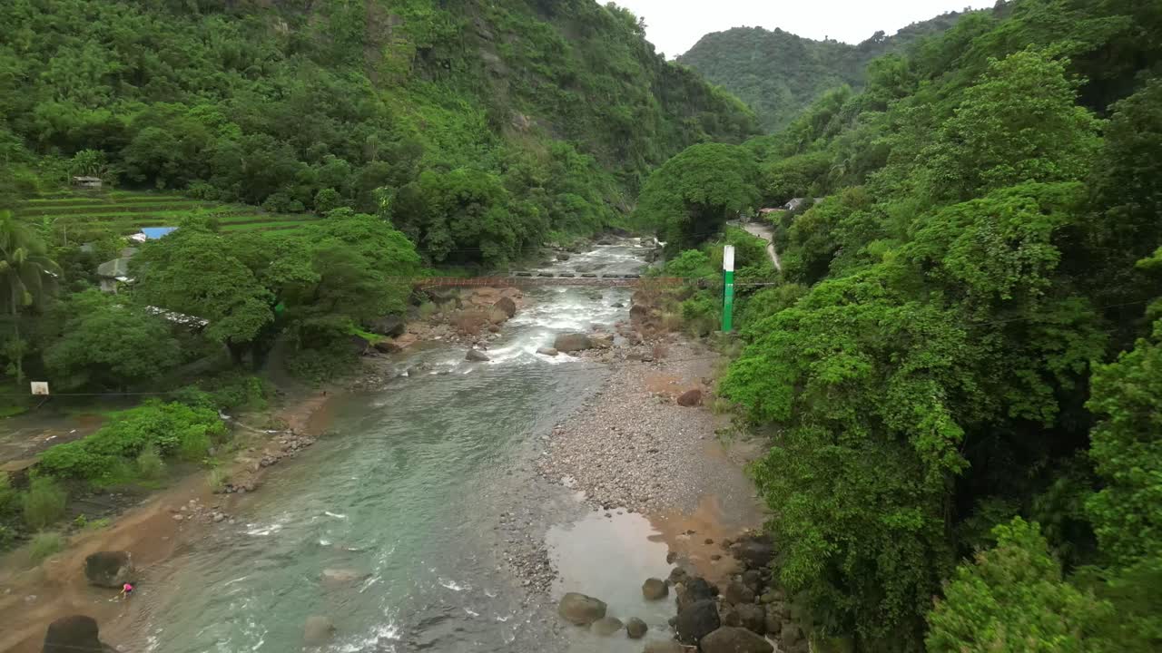 Aerial view of a clear river winding through a lush Philippine valley, with rocky banks, forested hills, and scattered homes nestled in vibrant greenery