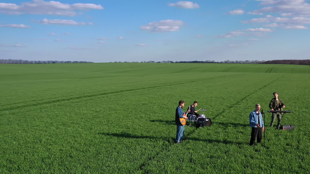 Group of young musicians on green field. Musical band performing music among nature in summer. Young people playing musical instruments. Aerial view.