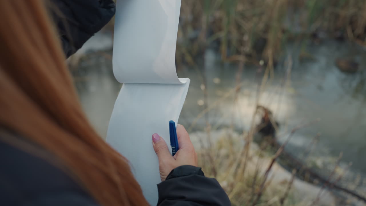 Dame controleert lange documenten nauwkeurig. Vrouw inspecteert en bladert zorgvuldig door vellen. Close-up van vrouw die meerdere papieren vellen nauwkeurig analyseert en doorbladert naast een moerasgebied.