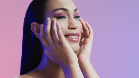 sonriente mujer biracial con cabello negro y maquillaje tocando su cara, copia espacio, cámara lenta