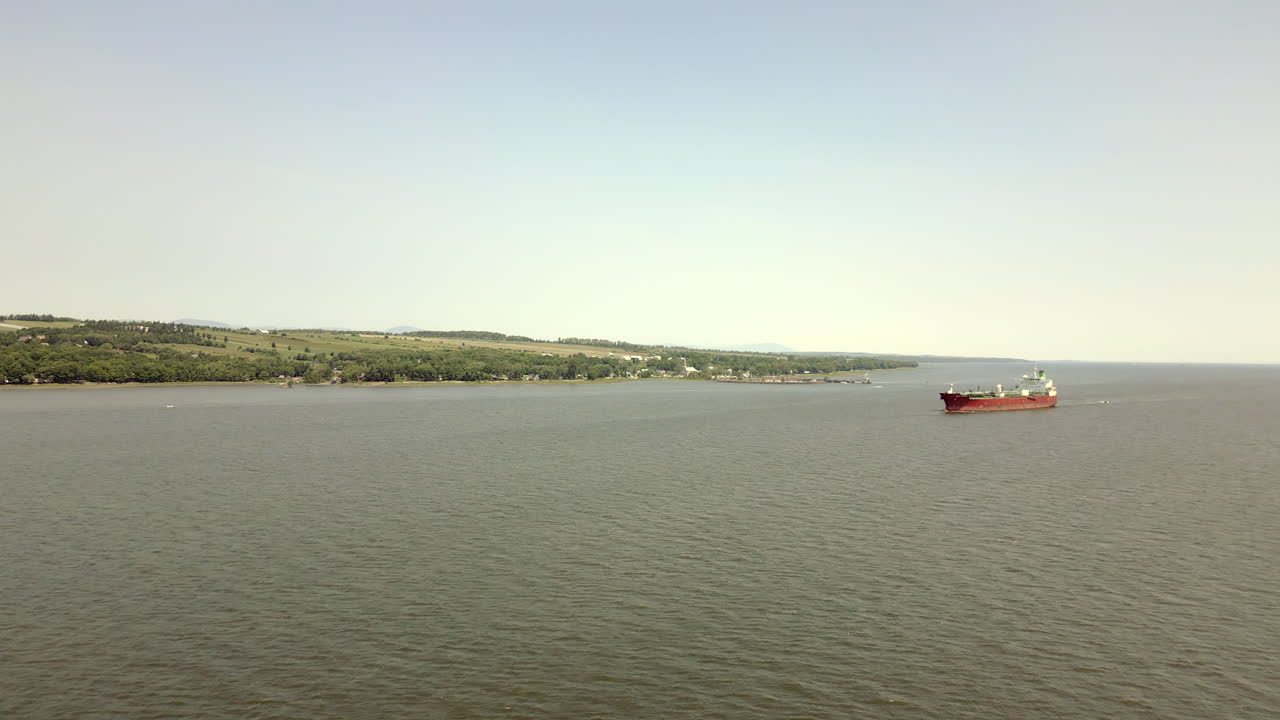 As you glide above the river, you'll be drawn towards a magnificent red cargo ship cruising gracefully, a testament to the bustling maritime activity of the region