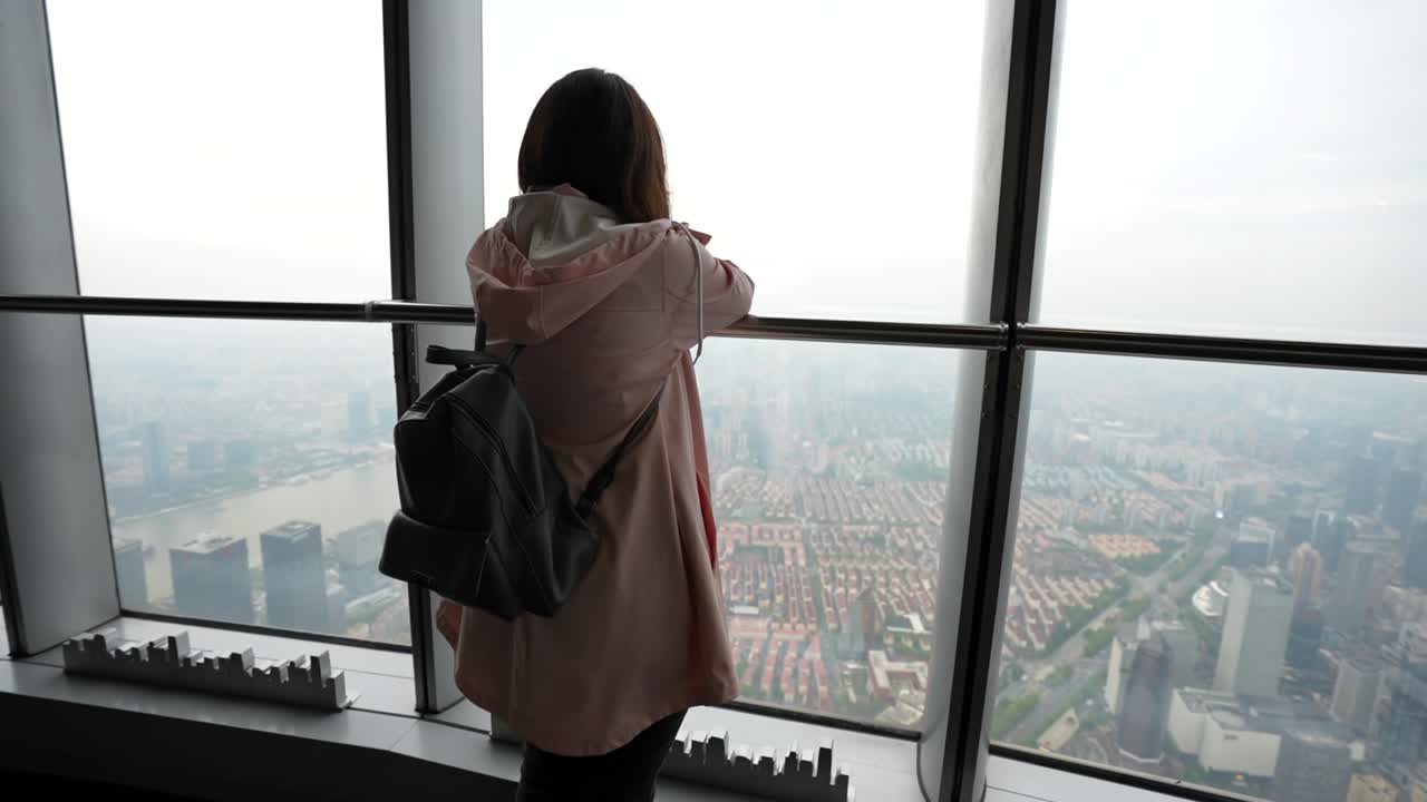 Rear slow motion of a visitor standing at Shanghai Tower observation deck watching the Huangpu River and city horizon unfold below, China