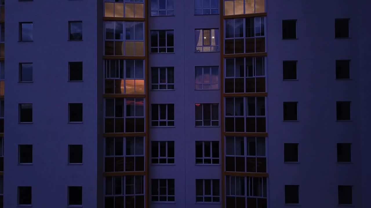 Drone view of colorful facade contemporary apartment building, windows and balconies. Aerial footage highrise estate at night time.