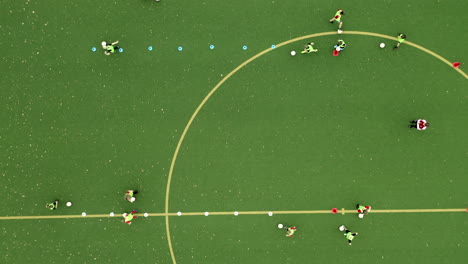 Los-Niños-Del-Campo-De-Fútbol-Verde-Juegan-Al-Fútbol-En-Una-Sesión-De-Entrenamiento-Con-El-Entrenador-4k-Drone-Topdown,-Vista-De-Pájaro